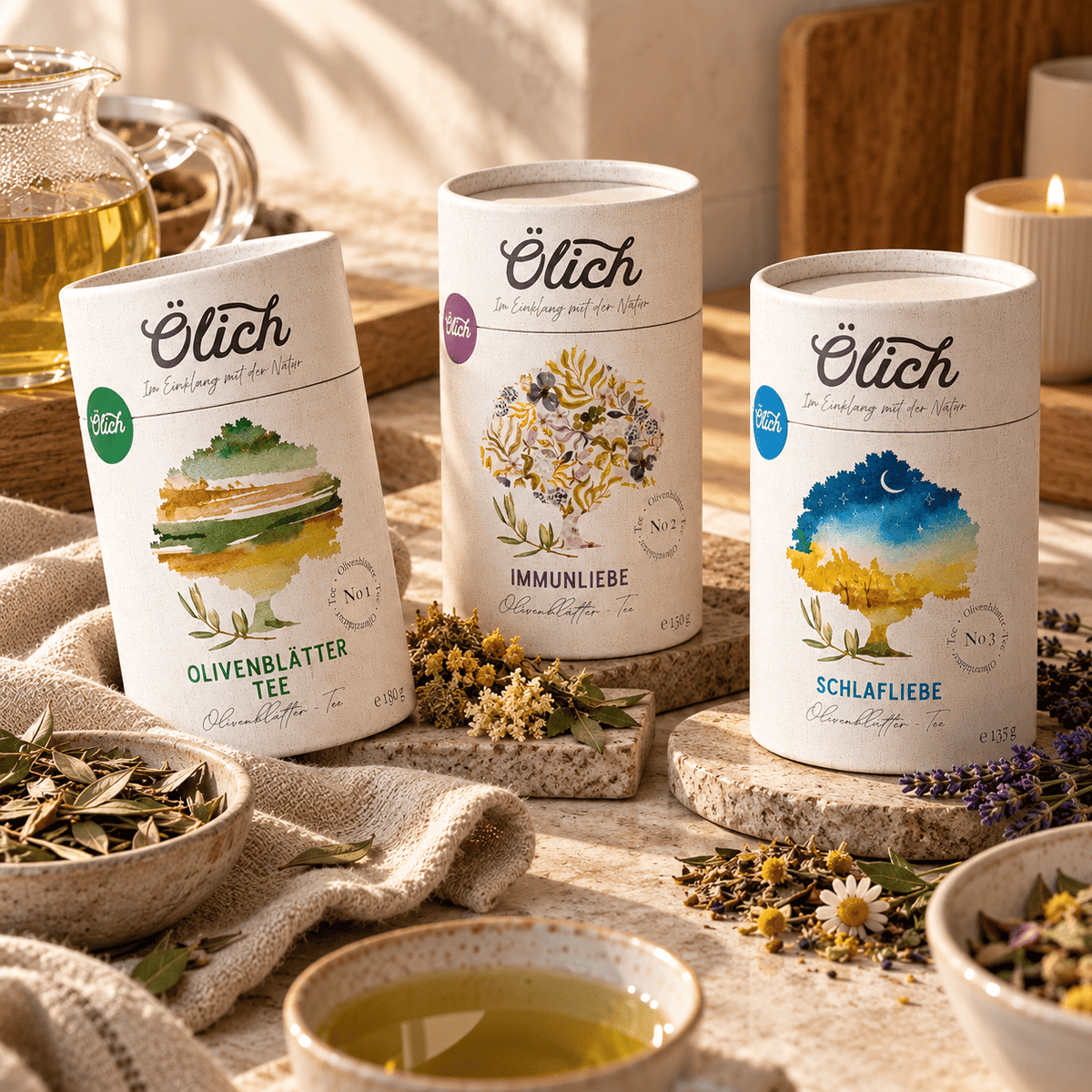 Die drei Ölich Teedosen mit Schalen voller loser Olivenblätter und Kräuterblüten, vorne eine Tasse Tee